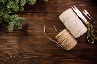 Makas, bükülmüş pamuk ip ve ladin dallarıyla süslenmiş koyu ahşap masa üzerinde çuval bezi ipi. El yapımı el işi kavramı, Noel ve kış tatili. Üst görünüm