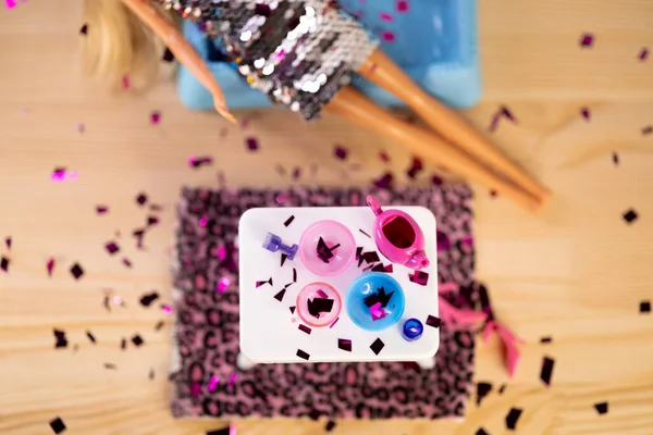 Pullu elbise giymiş yorgun bir bebek partiden sonra kaosun ortasında kanepede yatıyor. Servis masasının üst görüntüsü, dağınık topuklar ve dökülen konfetiler. 