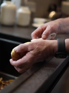 Patatesleri sebze soyucusuyla soyan adamın elleri. Evde yemek yapmak, sağlıklı yemekler, mutfak lavabosundaki çiğ patatesleri soymak. Yakın plan.