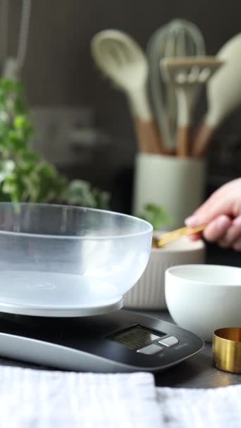キッチンスケールを使用してスプーンで小麦粉を振る女性の手 ベーキング 供給のための小麦粉の重量を量ること自宅で酸っぱい始動機 キッチンカウンターのスケール 小麦粉 — ストック動画