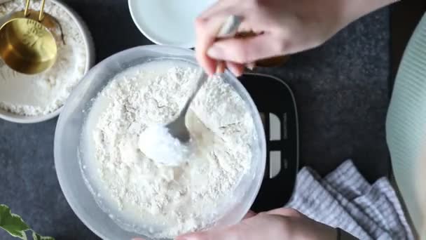 女性の手のトップビュー パンを焼くためのボウルに小麦粉と水を混ぜる 自宅で酸っぱいスターターを作るまたは供給 台所のスケール スプーンとカップの測定 — ストック動画