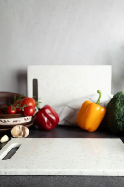 Canlı taze sebzeler, kiraz domatesleri, dolma biber, brokoli, sarımsak, mutfak tezgahında boş kesim tahtası. Sağlıklı yemekler, taze tarım ürünleri, organik ürünleri teşvik etmek, yerel gıda ürünleri