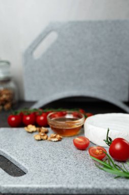 Yemek için aperatifler ya da malzemeler - Brie, ballı camembert, biberiye ve taş kesme tahtasında kiraz domatesleri. Mutfak tezgahında beyaz küflü yumuşak peynir. Boşluğu kopyala