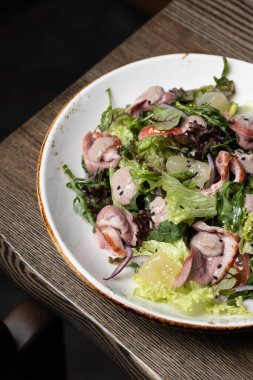 Ördek yakın plan ve beyaz tabakta salata, yeşiller, ahşap masada susam tohumları