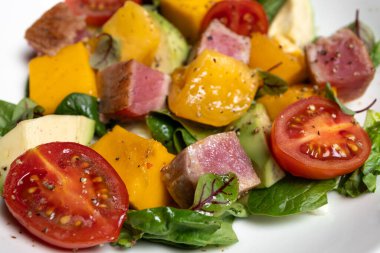 Rengarenk salata, ördek göğsü, mango ve domates küpleri yapraklı yeşillikler üzerine dizilmiş.