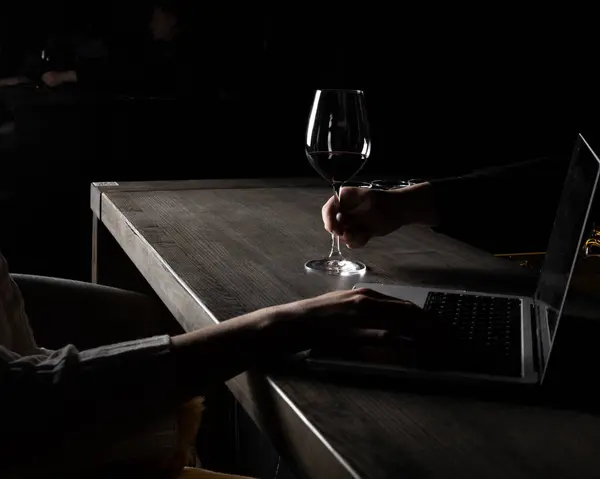 Barmenlerin dizüstü bilgisayarda klavye kullanan kadına bir bardak şarap verirken yakın plan. Karanlık ruh hali, gizem ve entrika hissi yaratmak. Boşluğu kopyala