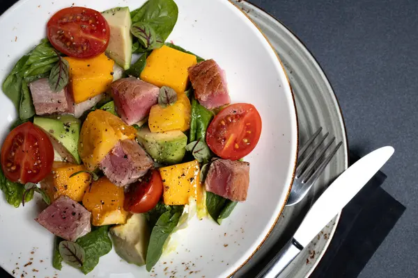 Beyaz tabakta taze salata, siyah peçete ve siyah arka planda gümüş çatal bıçak. İştah açıcı, sulu bir doku.