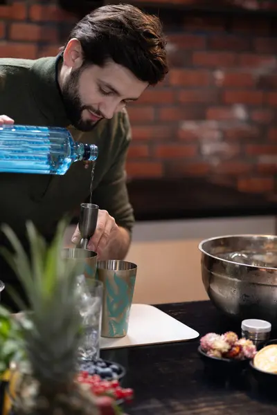 Barmen mavi şişeden kokteyl karıştırıcısına sıvı döküyor. Yakınlarda taze meyve ve bir kase buzla birlikte siyah tezgahın üzerinde titreyen. Boşluğu kopyala