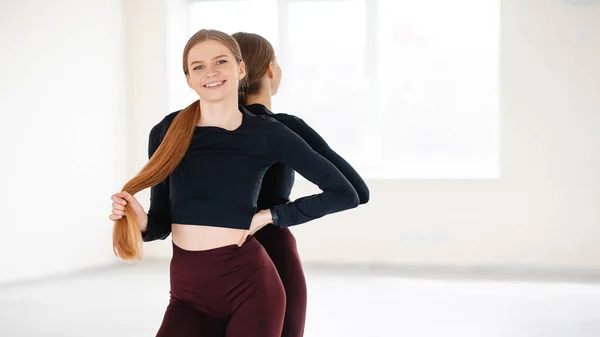 Sport, wellbeing and active lifestyle concept. Smiling pretty girl in sportswear, playing with ponytail and looking happy at camera after good gym workout, standing near mirros at white background