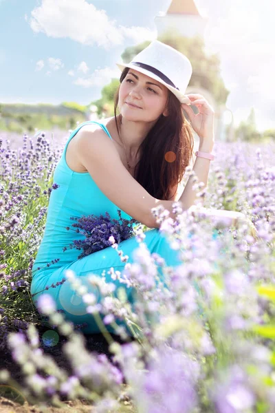 Elinde bir demet lavanta olan güzel, genç bir esmer kız lavanta tarlasında dinleniyor. Dikey.