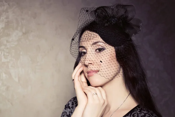 Portrait of a beautiful brunette in retro style. Delicate veil hat.