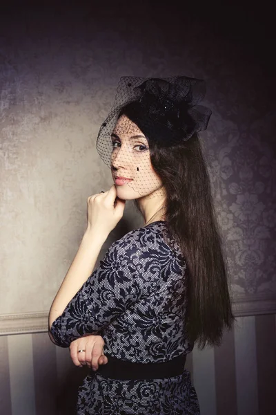Portrait of a beautiful brunette in retro style. Delicate veil hat.
