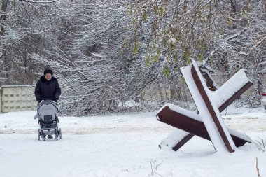 Ukrayna 'da kış. Lviv şehrinde bir caddede bir kadın bebek arabasıyla yürüyor. Sokağa bir anti-tank kirpi yerleştirildi. Ukrayna 'da savaş. 14.12.2022