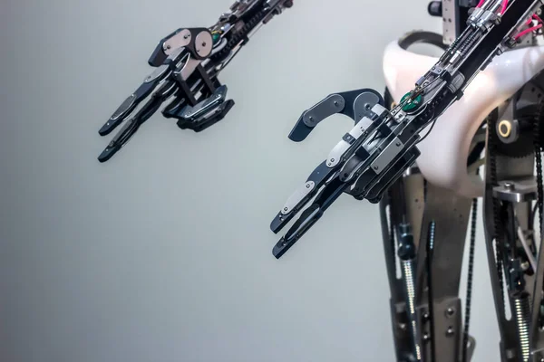 Humanoid robot hands. Metal fingers and knuckles with wires and springs. The robot shows a gesture - a gun. Gray blurred background. Place for text.