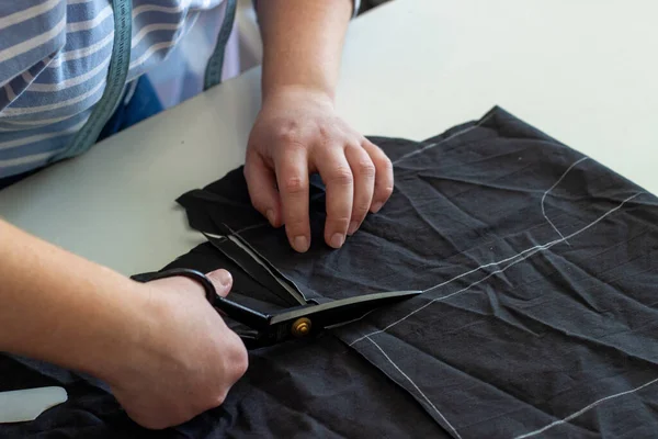 the process of cutting black fabric. Close-up of a seamstress\'s hands. Cutting and sewing courses. cutting of cloths. Horizontal