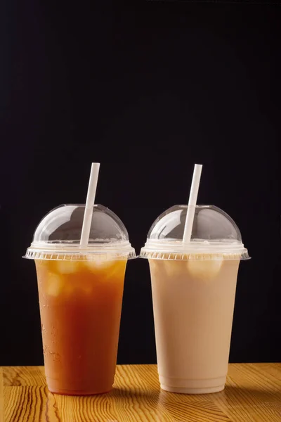 cold coffee cocktails. summer coffee-based refreshing drinks. Coffee and milk drink with ice cubes in plastic glasses with a plastic lid and straw. Summer mood. A drink in the heat. Vertical