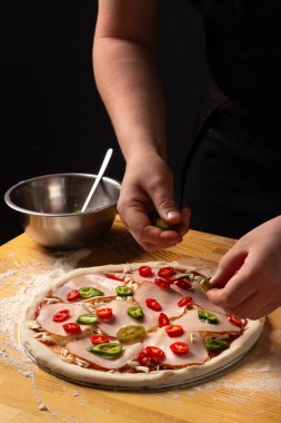 Pizza yapma süreci. Pizaiolla pizzaya jalapeno biberi sürer. Aşçının ellerine yakın çekim yap. İtalyan mutfağı. Baharatlı pizza. Pizza tarifi