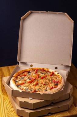 Açık bir karton kutuda pizza. Pizzacı, restoran menüsü. Dikey, koyu arkaplan.