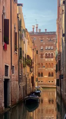 Dikey video. Venedik 'teki güneşli kanal manzarası. Sakin şehir Venedik. Dinlenmek ve turizm için harika bir yer. Eski şehrin sularındaki yansıma. 