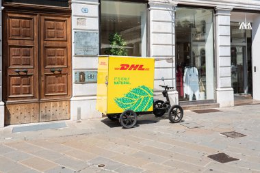 Padua, İtalya - 19 Haziran 2025: Lüks mağazaların yakınındaki işlek bir caddeye park edilmiş DHL elektrikli bisiklet Zara, güneşli bir yaz gününde fotokopi alanı ile canlı sarı renkler sergiliyor.