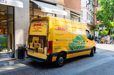 Padua, İtalya - 19 Haziran 2025: DHL dağıtım aracı lüks mağazaların yanındaki hareketli bir caddede park halinde, parlak sarı bir tasarım ve doğal motifler yer alıyor