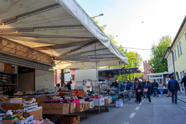 Montagnana, İtalya - 6 Nisan 2025: Çadırların altında ayakkabı ve mal satan satıcıların yer aldığı canlı bir açık hava pazarı, canlı bir kalabalığın göz gezdirme ürünleri ve olay yerini çevreleyen yeşillikler