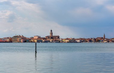 İtalya 'nın sakin rıhtım manzarasında ahşap direkler, büyüleyici binalar ve kilise kulesi yer alıyor ve seyahat meraklıları için pitoresk bir atmosfer yaratıyor.