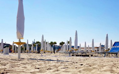 Plaj setinde beyaz şemsiyeler ve altın kumun üzerinde şezlonglar serin ve davetkar bir yaz atmosferi yaratıyor.