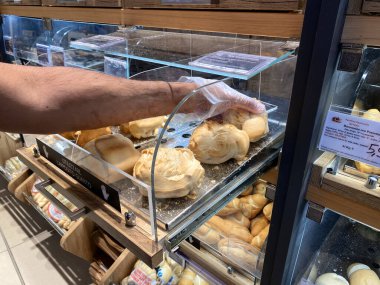 Conselve, İtalya - 16 Mayıs 2025: Müşterinin eli çeşitli fırın malzemeleriyle dolu bir fırın vitrininde taze ekmek rulolarına uzanıyor