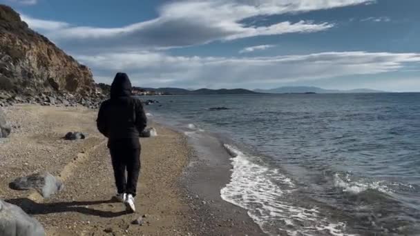 Man Wearing Hood Walking Alone Abandoned Beach Windy Day Beach — стоковое видео