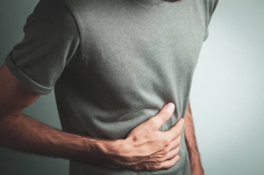 Adamın karnı ağrıyor. Gri bir arka planı var.