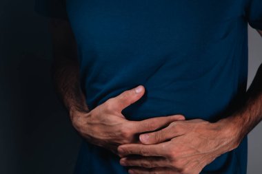 Midesini siyah arka planda tutan adam, kapat.