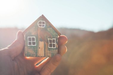 Bir adamın elinde küçük ahşap bir ev modeli..