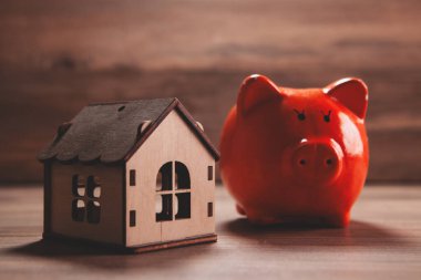 Ahşap bir maket üzerinde ev modeli ve tahta bir masa üzerinde bozuk paralar.