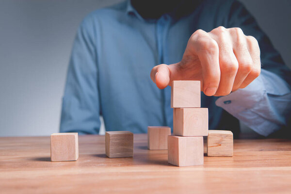 businessman hand stacking wooden cubes on wooden table