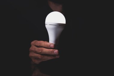 Siyah arka planda elektrik ampulü tutan erkek eli, alternatif enerji ve güç