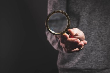 Siyah arka planı olan bir adam elinde büyüteç tutuyor.