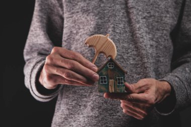 Mavi gömlekli adam ahşap bir ev modeli tutuyor..