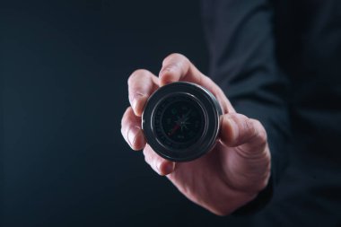 Koyu arkaplandaki pusulayı işaret eden iş adamı eli.