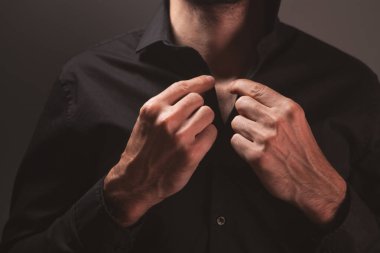 Genç bir adam koyu bir arka planda gömleğini ilikliyor. Ayarlanmış.