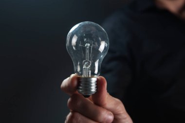 Karanlık arka planda bir ampulü tutan el. fikir kavramı