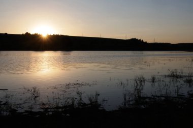 Kayıp bir gölde gün batımı. Güneş ışınları su yüzeyine düşer. Ufukta elektrik direkleri görünüyor..