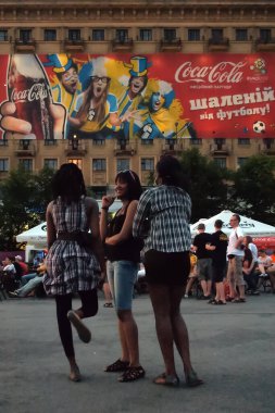 Kharkiv, Ukrayna - 12 Haziran 2012: Genç siyahi kadınlar Euro 2012 boyunca arka planda Coca-Cola pankartıyla yerel meydanda takılıyorlar. 