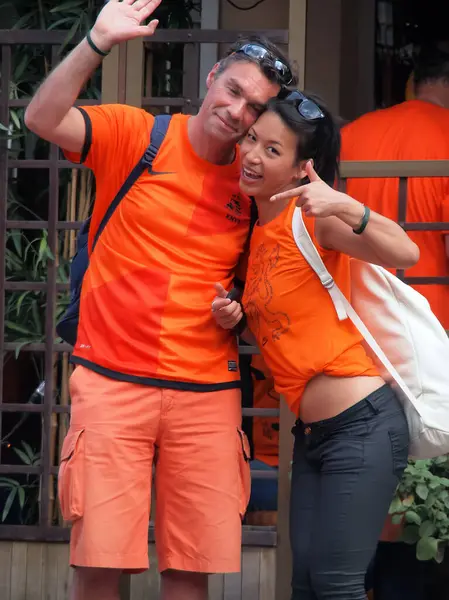 Kharkiv, Ukrayna - Haziran 09.2012: Turuncu elbiseli Hollandalı taraftarlar kafalarında gözlük ve sırt çantalarında fotoğraflarının çekildiğini gördüler. Kız gülümseyip el sallıyor, adam selamlamak için elini kaldırıyor..