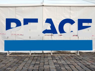 Huzur. Metal bir dağda mavi ve beyaz üç boyutlu dev harfler. Arkada, kırmızı ve beyaz bir şerit görebilirsiniz. Suç mahallini kordon altına almak için kullanılanla aynı. Yazıtın için aşağıda bir pankart var..