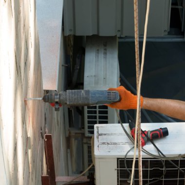 Bir işçi bir evin duvarına bir delik açar. Kızıl kaya tozu her yere uçar. Klimanın yanında yıpranmış matkap ucu olan yedek bir matkap var. İnşaatta yedek araçların kullanılması çalışma sürecinin gerekli bir unsurudur.