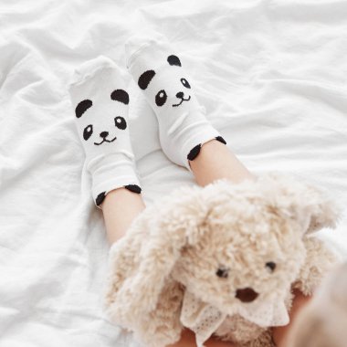 Bebek elinde pelüş bir oyuncak tutarken, yatağın üzerinde şirin panda çorapları giyerken.