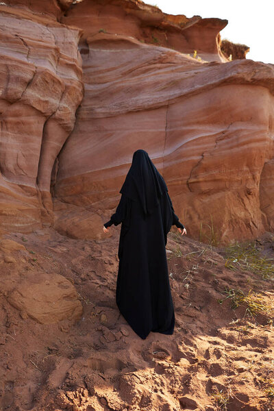 Muslim woman in national clothes and hijab walking in canyon