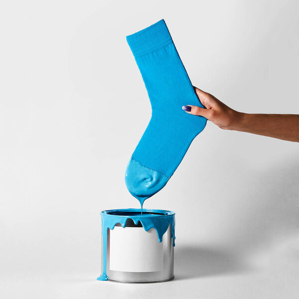 A female hand dips her blue sock into a can of paint