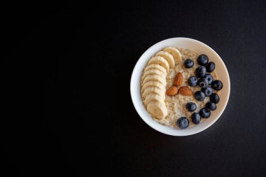 Muzlu yulaf ezmesi kasesi, badem ve yabanmersinli siyah arka plan izole edilmiş. Sağlıklı kahvaltı. Üst Manzara. Boşluğu kopyala